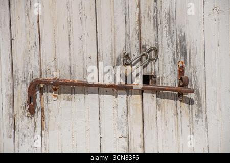 Rostiges altes Schiebeschloss und Haspe und Klammer an einem wetterbefallenen, schickem Holzeingang mit abblätterndem und abblätterndem Lack in einer alten ländlichen Scheune. Stockfoto