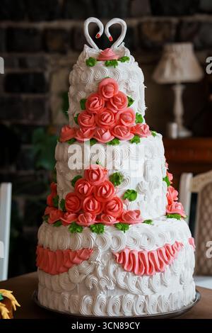 Eleganter dreistöckiger Hochzeitstorte mit Korallenrosen und Gusseisen, Herztopper, klassischer Feier, romantisches Dekor, weiß- und rosafarbene Farbtöne Stockfoto