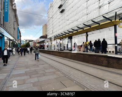 Manchester, Großbritannien - 17. September 2025: Fußgänger auf einer gepflasterten Marktstraße in Manchester, Großbritannien, mit Straßenbahnschienen und einem überdachten Bahnsteig. Stockfoto