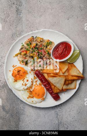 Ein schmackhafter und leckerer Frühstücksteller mit Eiern, Würstchen und knusprigen Tortilla Chips Stockfoto