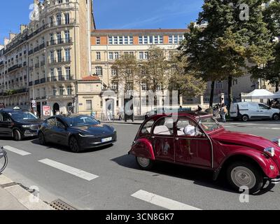 Paris, Frankreich. September 2025. Eine Straßenszene in Paris mit einem Vintage-roten Citroën 2CV und einem schwarzen Tesla-Elektrofahrzeug (EV), das am 6. September 2025 an einer Reihe eleganter Haussmann-Gebäude vorbeifährt. Fußgänger und andere Fahrzeuge teilen sich die breite Allee unter hellem, klarem Himmel. (Foto: Samuel Rigelhaupt/SIPA USA) Credit: SIPA USA/Alamy Live News Stockfoto