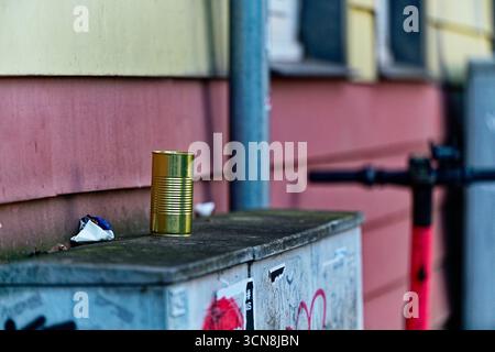 Eine mit Graffiti markierte Transformatorbox steht neben einem rot-gelben Haus mit einer Metalldose und Snackverpackungen in der Nähe, während ein gemieteter rosafarbener Roller wartet Stockfoto