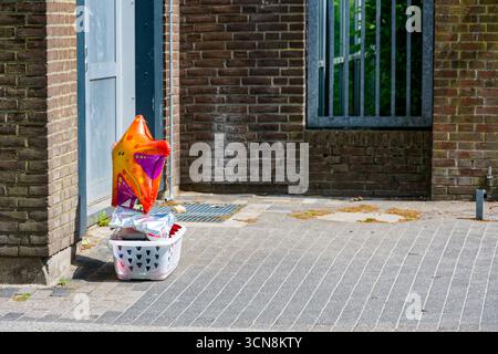 Ein verwittertes Backsteinhaus steht an einer grauen Holztür. Ein weißer Korb sitzt darunter und ein orangener Ballon hängt darüber. Die Szene deutet auf ein Giveaway-Kombo hin Stockfoto