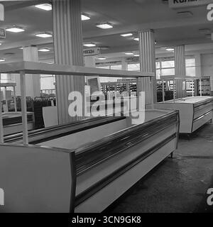 Ein historisches Foto aus dem Jahr 1983, das Reihen leerer Kühlvitrinen in der Lebensmittelabteilung des Kaufhauses „Universal“ in Sloviansk, ukrainische SSR zeigt. Die großzügige Verkaufsfläche mit Schildern für "Getränke" und "Mineralwasser" steht im Kontrast zum Mangel an Waren, ein markantes Symbol für die Rohstoffknappheit in der späten sowjetischen Wirtschaft. Das Bild spiegelt die alltäglichen Realitäten und das Leben des sowjetischen Handels wider. Stockfoto