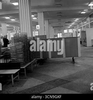 Ein historisches Foto aus dem Jahr 1983, das die Verkaufsfläche der Lebensmittelabteilung im Kaufhaus „Universal“ in Sloviansk, ukrainische SSR, zeigt. Im Vordergrund befinden sich hohe Stapel von Metallkörben, und im Hintergrund der Halle mit Säulen sind Schilder für Abteilungen wie „Würstchen“, „Fette“ und „Kuchen“ zu sehen. Das Bild vermittelt die authentische Atmosphäre und das tägliche Leben eines großen sowjetischen Selbstbedienungsgeschäfts Stockfoto