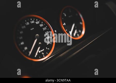 Das Armaturenbrett des Fahrzeugs mit leuchtenden orangefarbenen Ringen beleuchtet den Tachometer und andere Anzeigen und zeigt die Geschwindigkeit und den Fahrzeugstatus bei Nachtfahrten an Stockfoto