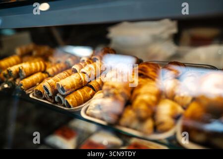 Bäckerei-Vitrine gefüllt mit verschiedenen frisch gebackenen Gebäckstücken – goldene Croissants, Schokoladencreme-Brötchen und Cannoli – verlocken Kunden mit Wwa Stockfoto