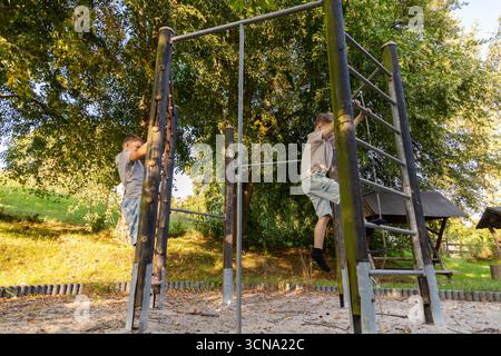 Zwei Kinder spielen fröhlich in einer natürlichen Umgebung, klettern auf Spielgeräten und genießen die Natur an einem sonnigen Tag. Stockfoto