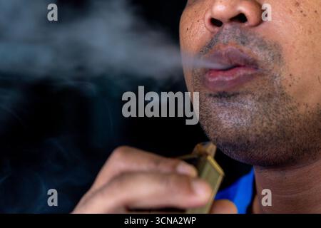 Ein Mann, der Dampf aus einer E-Zigarette oder einem Vape ausatmet. Dampfkonzept, Rauchen. Stockfoto