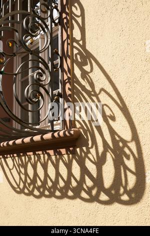 Dekorativer, lockiger Eisengitter an einem Fenster, das lange Schatten auf eine gelbe Wand wirft, in der Altstadt, Freiburg im Breisgau, Deutschland. Stockfoto
