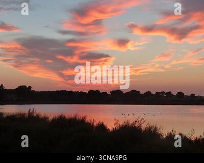 Ein wunderschöner Sonnenuntergang auf Mallorca mit zarten Orange- und Rosa-Tönen, die sich auf einem ruhigen See spiegeln, eingerahmt von dramatischen Wolkenformationen am Himmel Stockfoto