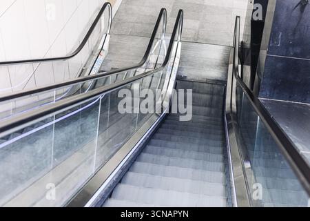 Rolltreppe im Innenbereich. Moderne, bewegliche Treppe im Einkaufszentrum. Städtisches Verkehrssystem für Menschen. Architekturdetails mit Stahl und Glas. Stockfoto