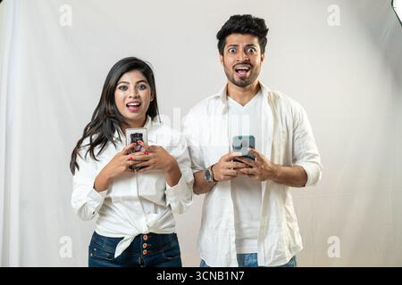 Ein schockiertes Paar, das sich ihre Handys ansieht. Stockfoto