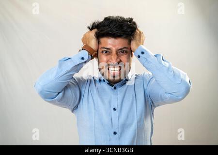 Ein junger Mann, der in Not seinen Kopf mit frustriertem Ausdruck hält. Stockfoto