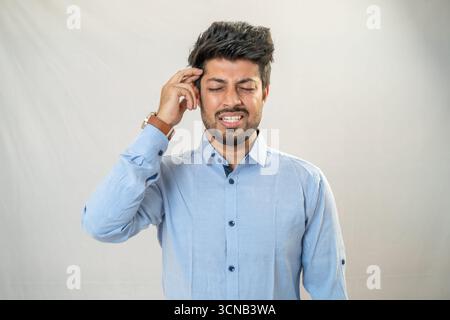 Ein junger Mann mit einem ernsten, nachdenklichen Ausdruck, der seine Stirn berührt. Stockfoto