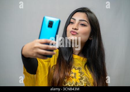 Eine junge Frau, die ein Selfie mit einem hellblauen Handy macht und ein Küssgesicht macht. Stockfoto