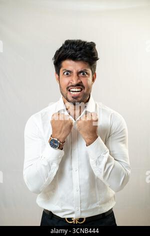 Ein junger Mann in einem weißen Hemd mit einem intensiven, fröhlichen Ausdruck. Mann, Der Intensive Emotionen Ausdrückt - Studio Portrait Stockfoto