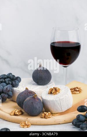 Käse, Feigen und Nüsse auf einem Holzbrett mit einem Glas Rotwein Stockfoto