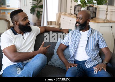 Afroamerikaner Vater und Sohn sprechen auf grauem Sofa im Wohnzimmer mit schwarzen Laternen Stockfoto