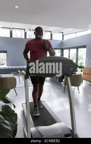 Ranghoher afroamerikaner, der Sportswear trägt, läuft auf Laufband im Wohnzimmer Stockfoto