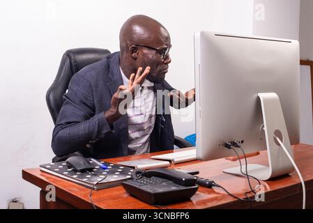 Ein Geschäftsmann in Jackett, der am Schreibtisch sitzt und am Computer arbeitet, sieht unglücklich aus. Stockfoto