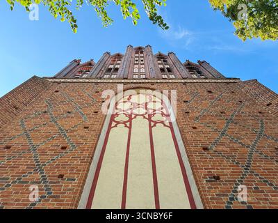 Aufwärtsaufnahme der historischen gotischen Backsteinkirchfassade aus dem Jahr 1370 in Europa mit gemalten vertikalen Abschnitten und Fensterdetails. Stockfoto