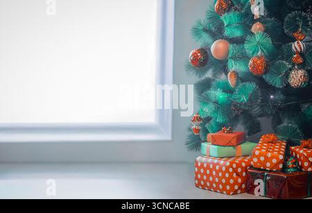 Festliche Geschenke und ein Weihnachtsbaum neben einem großen Fenster Stockfoto
