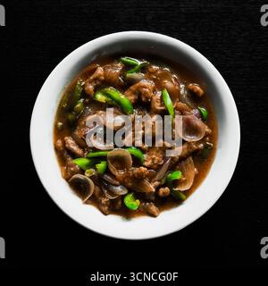 Herzhaftes, gebratenes Rindfleisch mit grüner Paprika und Zwiebeln in kräftiger brauner Sauce, serviert in einer traditionellen weißen Schüssel für eine authentische asiatische Mahlzeit Stockfoto
