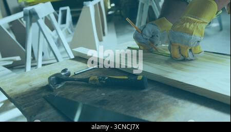 Mit Handschuhen markierende und messende Planke auf Werkstatttisch, mit Lineal, Sägeblatt und Hammer Stockfoto