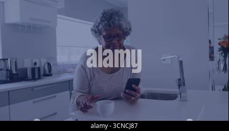 Smartphone in der Hand, Seniorin berührt Kaffeetasse auf der modernen Kücheninsel, mit orangefarbenen Blumen Stockfoto