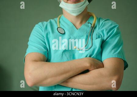 Nahaufnahme eines Arztes mit Schutzmaske und Stethoskop, stehend mit gekreuzten Armen. Medizinischer Fachmann, Gesundheitskonzept, Krankenhausumgebung, vertrauenswürdiger Arzt. Stockfoto