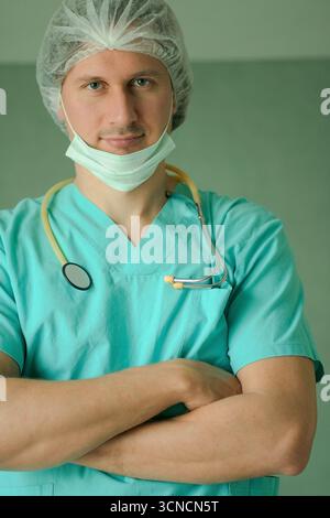 Nahaufnahme eines erfahrenen männlichen Arztes mit medizinischer Maske und Stethoskop, stehend mit überkreuzten Armen. Konzept der Gesundheitsversorgung, medizinische Professionalität, vertrauenswürdiges klinisches Personal. Stockfoto
