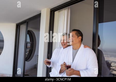 Verschiedene Seniorenpaare tragen Bademäntel mit Bechern, die auf dem Balkon in der Nähe des Fensters liegen Stockfoto