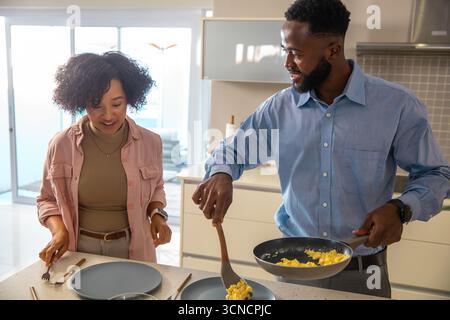 Verschiedene Paare halten Pfanne und Spachtel, kochen Rührei auf der Arbeitsplatte in der Küche Stockfoto