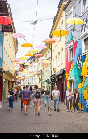 Bunte Schirmstrassenszene mit Fußgängern und hellen Wandmalereien in der charmanten Stadt Villach, Österreich Stockfoto