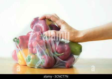 Eine Hand berührt einen wiederverwendbaren Netzbeutel, der mit bunten Paprika gefüllt ist. Konzept bewusster Konsumgewohnheiten und gesunder pflanzlicher Ernährung Stockfoto