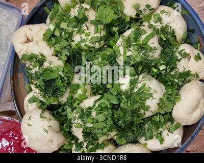 Eine rustikale Schüssel gefüllt mit frisch gedämpftem Varenyky (Knödel), bestäubt mit gehackten frischen grünen Kräutern, auf einer Küchenzeile. Der sanfte Dampf r Stockfoto