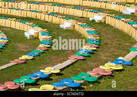 Amphitheater-Sitzgelegenheiten mit hellen, blumenförmigen Hockern aus rotem, blauem, grünem und gelbem Beton, in geschwungenen Reihen im Freien auf grasbewachsenem Boden in d Stockfoto