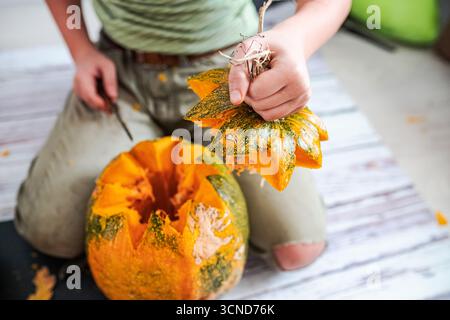 Eine Person schnitzt einen großen Kürbis, der seinen Stiel hält. Stücke von orangefarbenem Kürbis sind verstreut. Es ist wahrscheinlich Herbst und bereitet sich auf Halloween vor Stockfoto