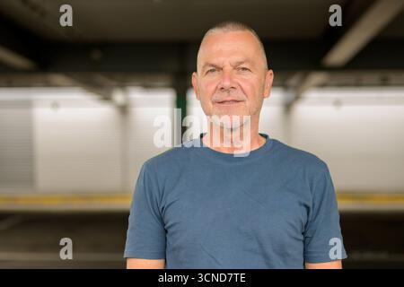 Porträt eines selbstbewussten älteren Mannes mit kurzen grauen Haaren und beschnittenem Bart, mit einem einfarbigen blauen T-Shirt. Stockfoto