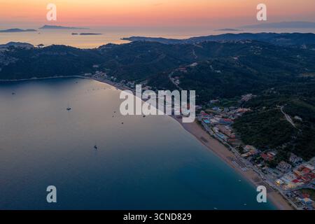 Panoramablick auf die Bucht von Agios Georgios in Korfu, Griechenland, während eines herrlichen Sonnenuntergangs. Der Himmel leuchtet orange und rosa über dem Ionischen Meer, sil Stockfoto