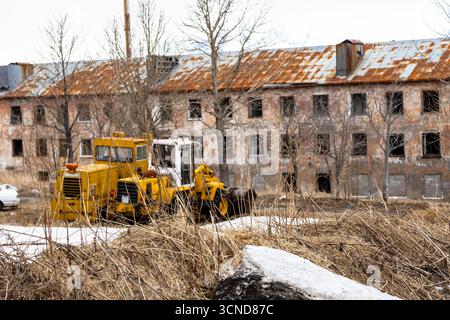 Getrocknetes Gras und Traktor mit verlassenem Wohngebäude im Hintergrund in Petropavlovsk-Kamtschatski Stadt am Frühlingstag, Region Kamtschatka, Russland Stockfoto