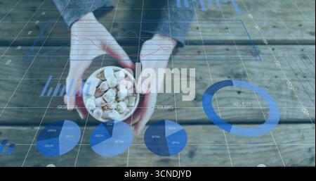 Hände im Pullover mit Schüssel mit Marshmallows und Schokolade auf Holztisch, mit digitalen Karten Stockfoto
