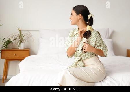 Eine schöne Frau, die im Schlafzimmer einen Pferdeschwanz mit Scrunchies macht Stockfoto