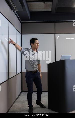 Präsentator steht neben Whiteboard und Podium, mit Laptop, Gesten im Besprechungsraum Stockfoto