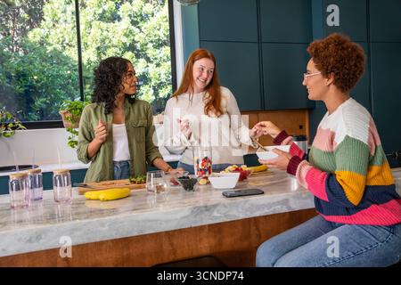 Verschiedene Freundinnen hacken Erdbeeren in der Küche mit dem Mixer für Smoothie Stockfoto