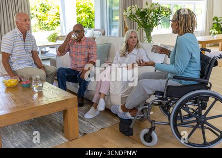 Seniorenfreunde plaudern um einen Couchtisch im Wohnzimmer, knacken Chips, trinken Wasser Stockfoto