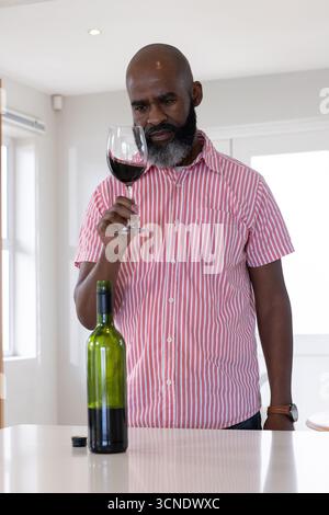 Ranghoher Afroamerikaner, der Rotwein im Stielglas an der modernen Küchentheke untersucht Stockfoto