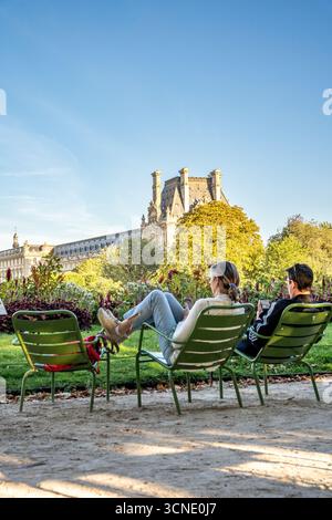 Zwei Personen entspannen sich auf grünen Stühlen bei Sonnenuntergang im Jardin des Tuileries, mit Blick auf den historischen Louvre im Hintergrund, Paris, Frankreich Stockfoto