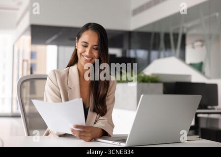 Glückliche junge Juristin, die am Arbeitsplatz Papier liest Stockfoto